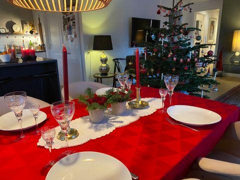 Et dækket julebord med rød dug og et pyntet juletræ i baggrunden