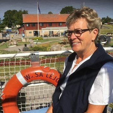 Lone med kort hår, briller og hvid t-shirt sidder og smiler fordi hun lykkedes med at finde frivillige personer til Mødrehjælpen gennem Boblberg platformen