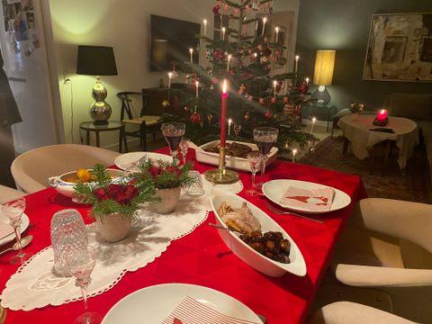 Et dækket julebord med rød dug og et pyntet juletræ i baggrunden