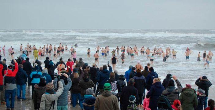 En stor flok mennesker løber i det kolde vand påp stranden