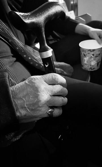 Et sort/hvid billede af en gammel dames rynkede hænder og hendes stok, som hun holder i hånden
