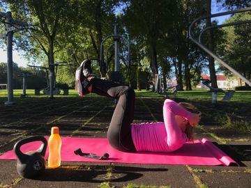 En kvinde i pink sportstøj ligger på en yogamåtte og træner yoga udenfor