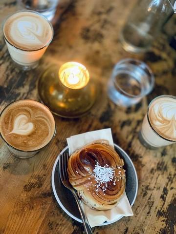 Et café bord med en kanelsnegl og et stearinlys og to kopper kaffe